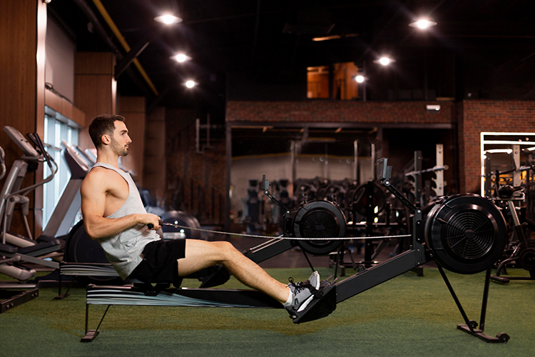 Man with the Wolf chronotype exercising on a rowing machine in the gym in the evening