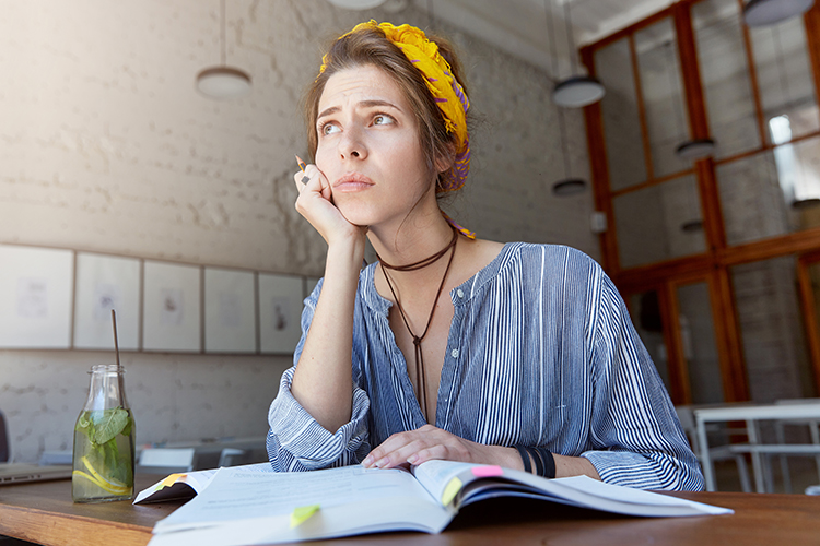 Woman with the Dolphin chronotype sitting at a table with an open book and pencil, looking thoughtfully to the side