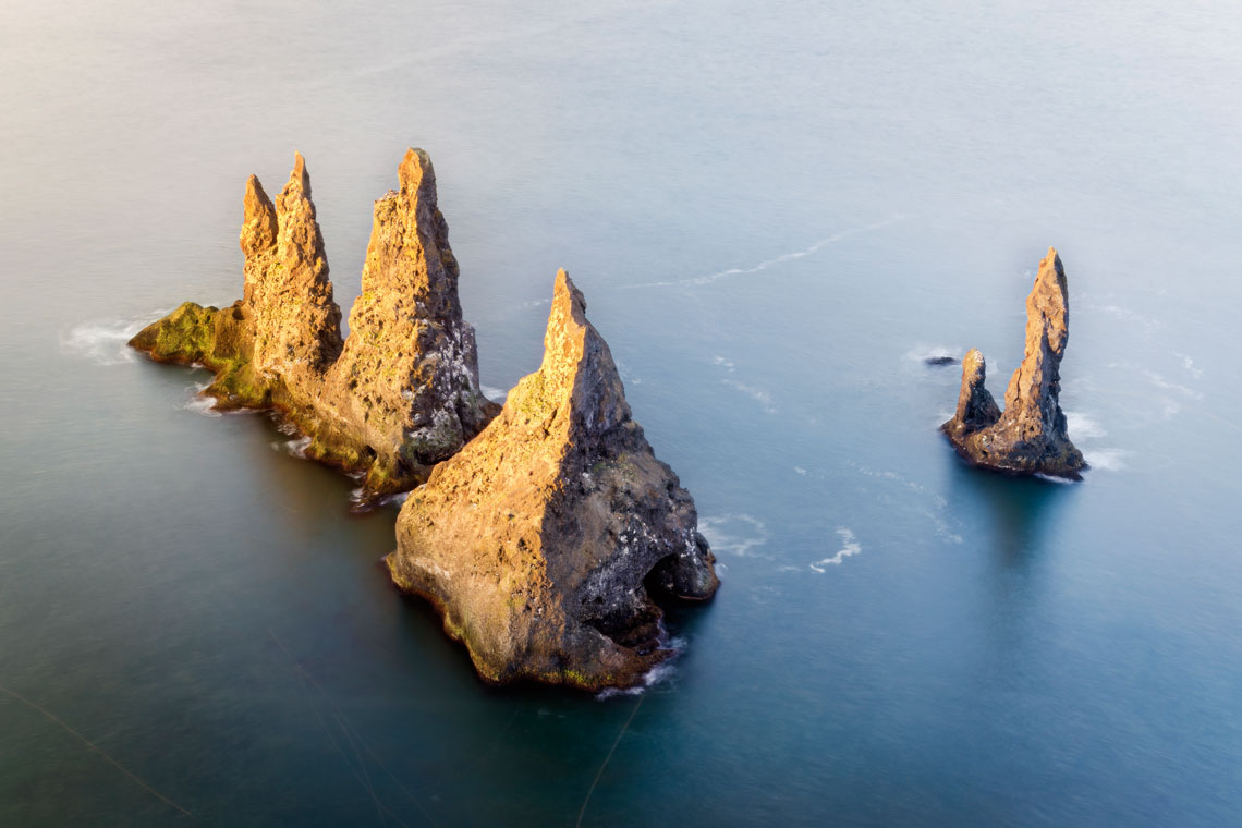 Near Mount Reynisfjall are the famous basalt kekurs (cone-shaped rocks) – Reynisdrangar. They are several tens of meters away from the beach of Reynisfiyara and are washed by the waters of the Atlantic Ocean. According to one of the local legends, these picturesque pillar-shaped rocks appeared when two trolls tried to pull a three-masted ship ashore, which had run aground. But as the sun rose, daylight broke through the clouds and the trolls petrified to form kekurs.